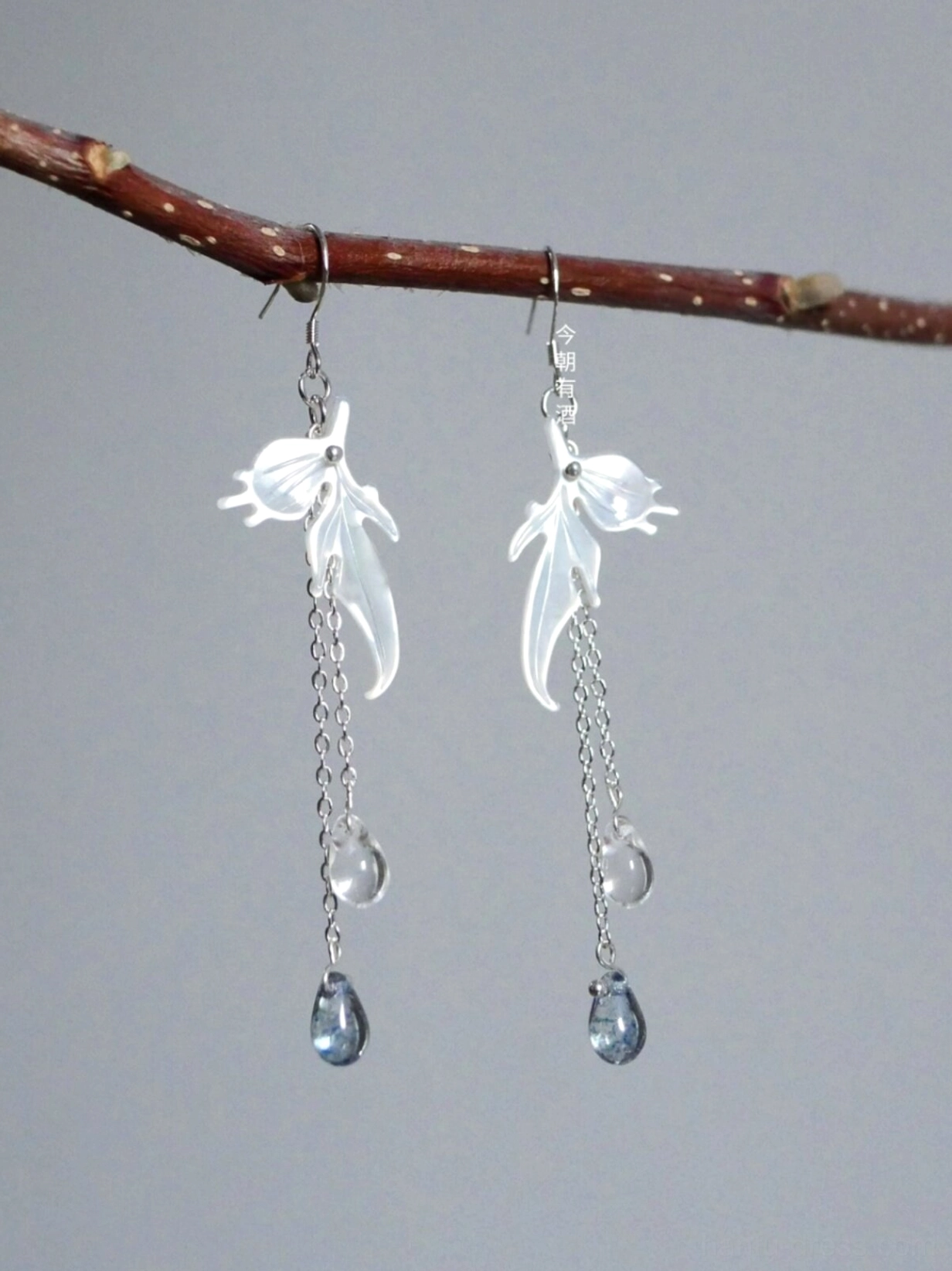 Goldfish themed Chinese dangle earrings with silver ear hooks, iridescent white fish pendants, clear beads, and dark blue teardrop charms