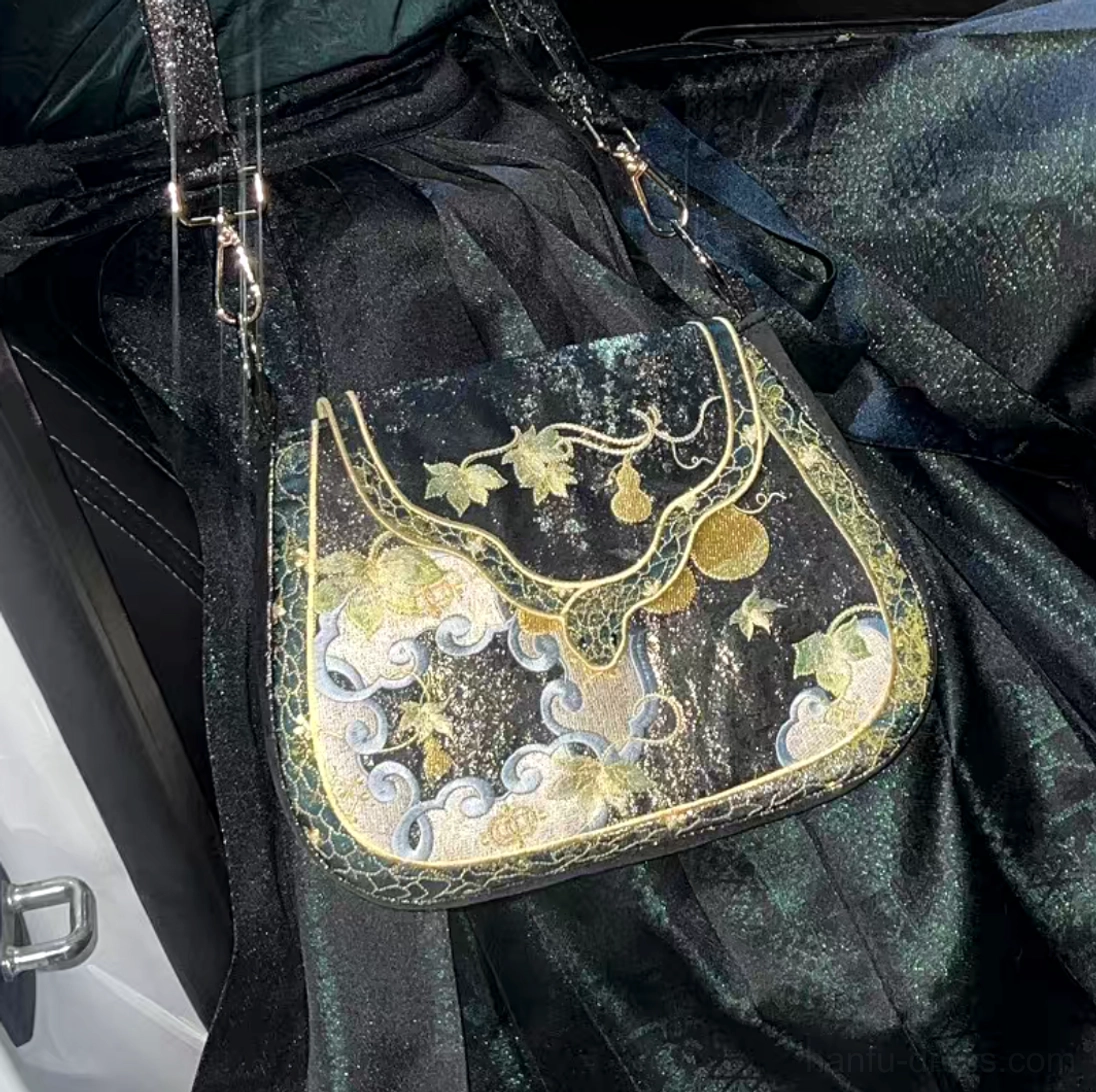 Gold gourd and cloud embroidered traditional Chinese saddle bag worn crossbody with dark green Hanfu, showing metal strap hardware