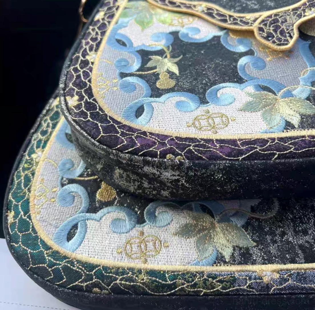 Close view of embroidered Chinese saddle crossbody bags with gold gourd cloud patterns and purple and green decorative trim
