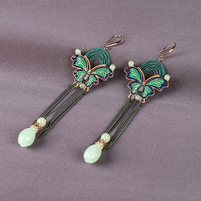 Angled flat lay view of green blue enamel butterfly teardrop earrings with black chain fringe and light green pendants