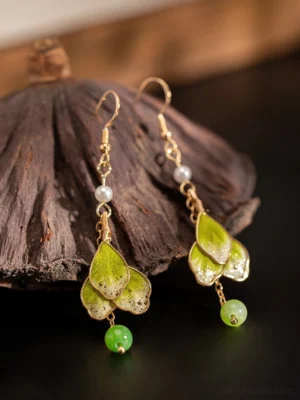 Hook-style green floral Hanfu earrings with gold chain details, white pearl and green bead pendants arranged beside a dried lotus pod