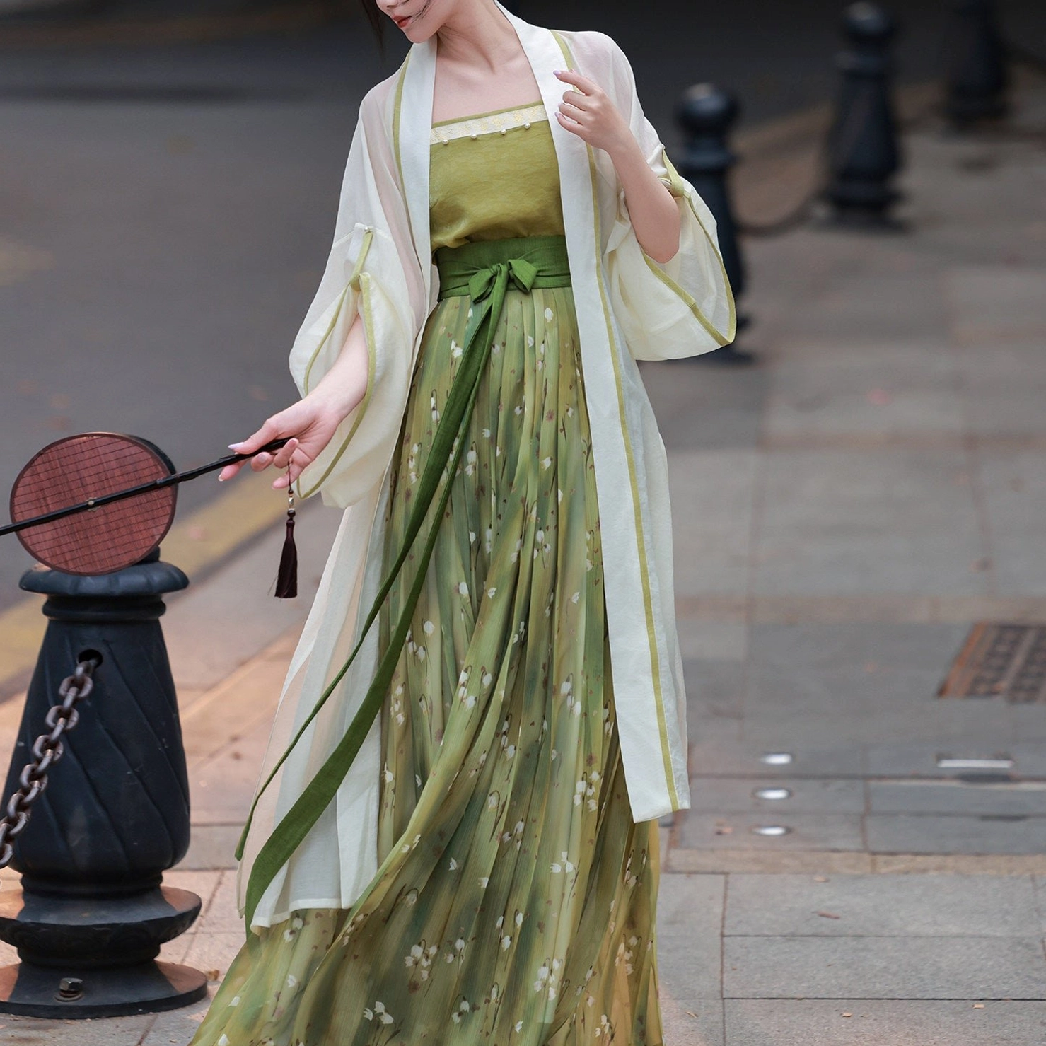 Front close-up of green floral Song Dynasty Hanfu full set with sheer cardigan, camisole, pleated skirt and traditional round fan