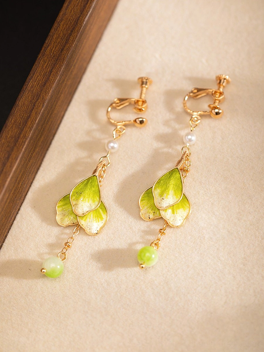 Green gradient flower dangle Chinese earrings with gold-tone clip-on fittings, white pearl and green bead accents displayed on a beige mat