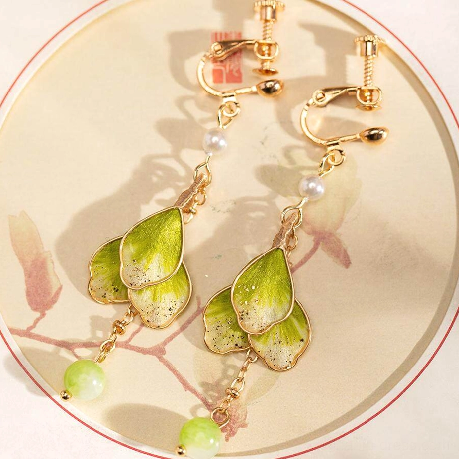 Two pairs of green and gold Chinese flower earrings showing both hook and clip-on styles on a traditional floral patterned tray