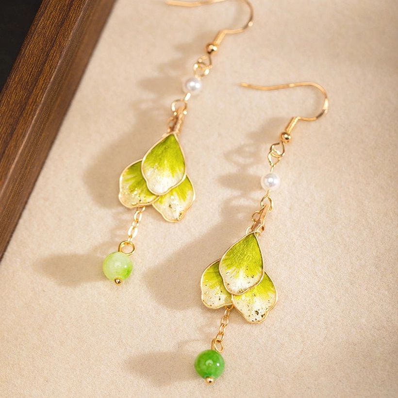Green gradient petal Chinese hook earrings with gold edging, white pearl and matching green bead shown on a linen display board