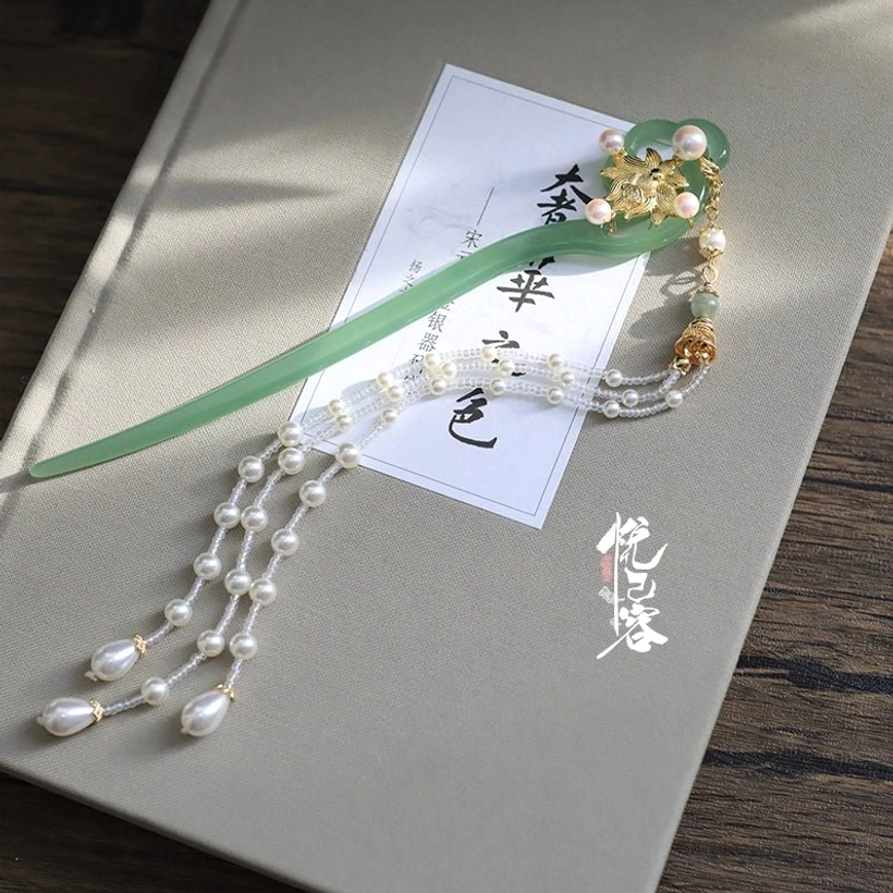 Green jade-toned Chinese hair pin with gold floral ornament, freshwater pearl tassel, and matching jade bead accents displayed on a vintage Chinese calligraphy notebook
