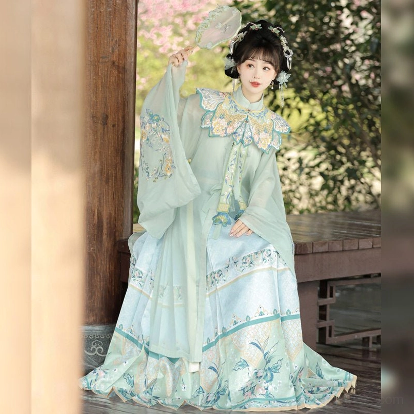 Light cyan and green-toned Ming Dynasty summer Hanfu set with flowing embroidered robe, traditional mamian skirt, floral cloud collar, and folding fan in a pavilion