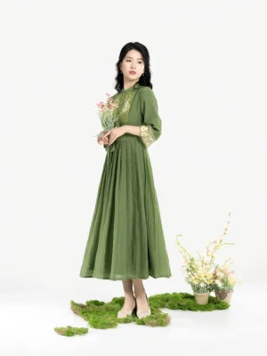 Three-quarter front view of a green modern Hanfu Tencel pleated dress with stand collar, three-quarter sleeves, traditional embroidered chest motifs, embroidered cuffs, matching waist sash, and flowing A-line skirt