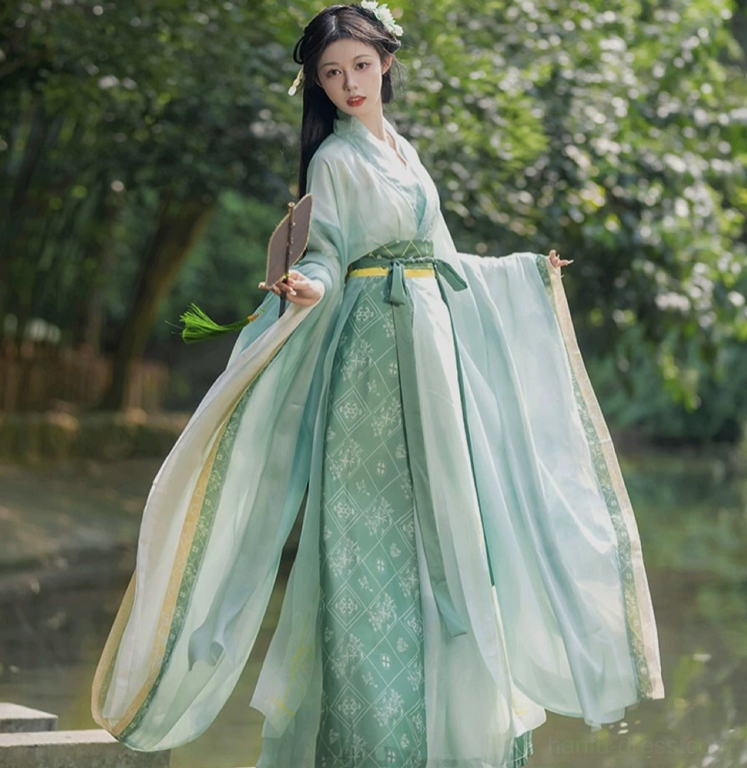 Side view of a green Qiyao Ruqun Hanfu with layered mint and dark green fabric, wide flared sleeves, handheld fan, and classical floral hair ornaments