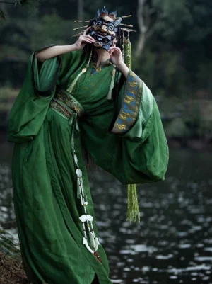 Green Warring States and Han Dynasty straight hem Hanfu robe shown from a three quarter front view on a female model beside a lake, featuring wide sleeves, blue and gold embroidered trim, a jade tassel waist pendant, and traditional fantasy styling