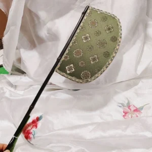 Green half-moon Chinese hand fan with floral brocade fabric gold braided trim and dark bamboo handle held in hand