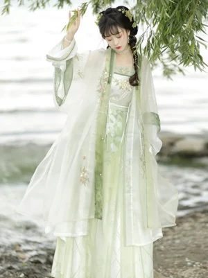 Green and white Song Dynasty style Hanfu with floral embroidered bust, decorative waist sash, and layered beizi coat by a lakeside