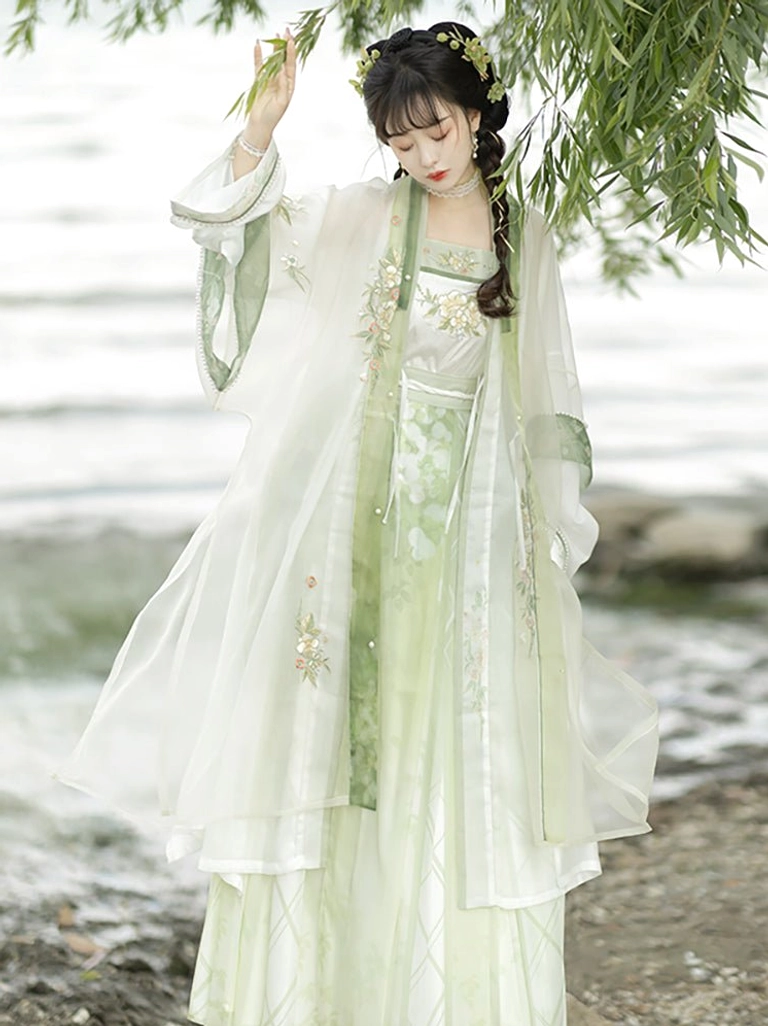 Green and white Song Dynasty style Hanfu with floral embroidered bust, decorative waist sash, and layered beizi coat by a lakeside