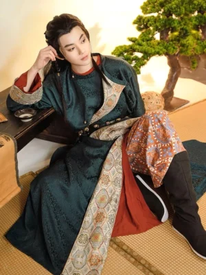 Side seated view of Guan Shan Yue men’s Tang Hanfu outfit showing patterned trousers, brocade collar trim, layered robe, and traditional waist styling