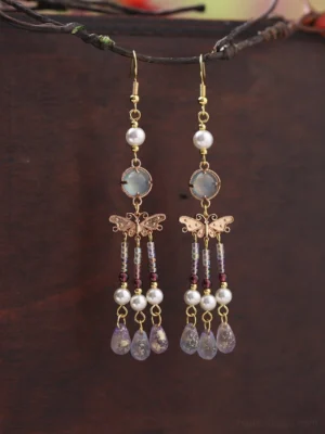 Chinese butterfly dangle earrings hanging from a tree branch, featuring pearl accents, opalescent blue stones, gold-tone details, beaded tassels, and purple teardrop pendants