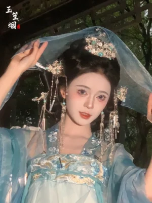 Model wearing Hall of Eternal Life phoenix turquoise tassel Hanfu hair accessory set with cyan embroidered Hanfu and sheer blue veil in an outdoor wooden pavilion