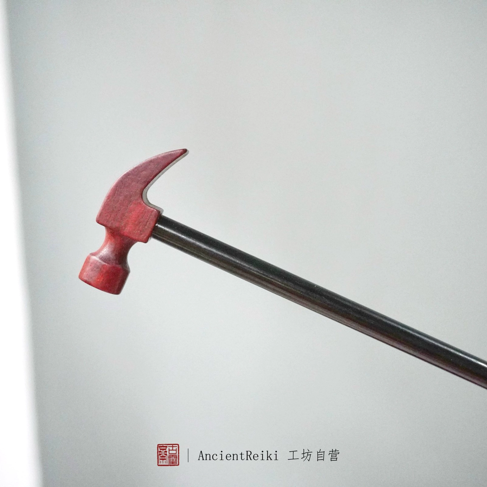 Full side profile of a claw hammer shaped Chinese hair stick in reddish-brown and dark wood tones