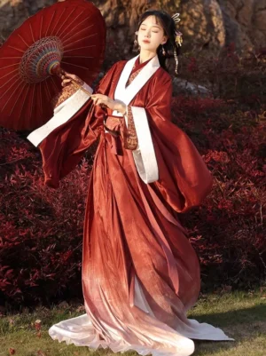Front view of a woman wearing a gradient deep red and soft pink Han Dynasty Hanfu straight hem robe with wide sleeves, white contrasting collar and cuffs, brocade trim, flowing skirt, and long waist sash in an autumn garden