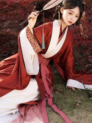 Side view of a woman in a traditional Han Dynasty Hanfu straight hem robe with wide sleeves, visible white inner layer, trailing pink waist sash, vintage hair ornaments, and feather fan outdoors