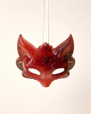Hand-carved red brown natural agate fox spirit mask pendant for a traditional Chinese necklace on a soft pink background
