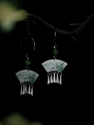 Hand-painted orchid fan-shaped Chinese earrings with green beads and silver tassels shown in a close-up view with soft green foliage