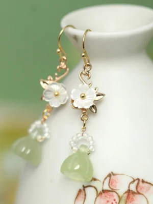 Handcrafted lotus pod Hanfu earrings displayed on a ceramic vase with gold-toned hardware white flowers and green botanical pendants
