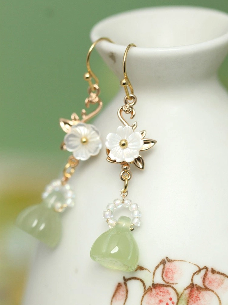 Handcrafted lotus pod Hanfu earrings displayed on a ceramic vase with gold-toned hardware white flowers and green botanical pendants