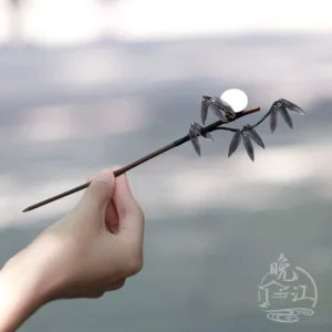 Hand holding an elegant bamboo moon hair stick with traditional Chinese bamboo branch decoration, dark wooden shaft, and white moon accent