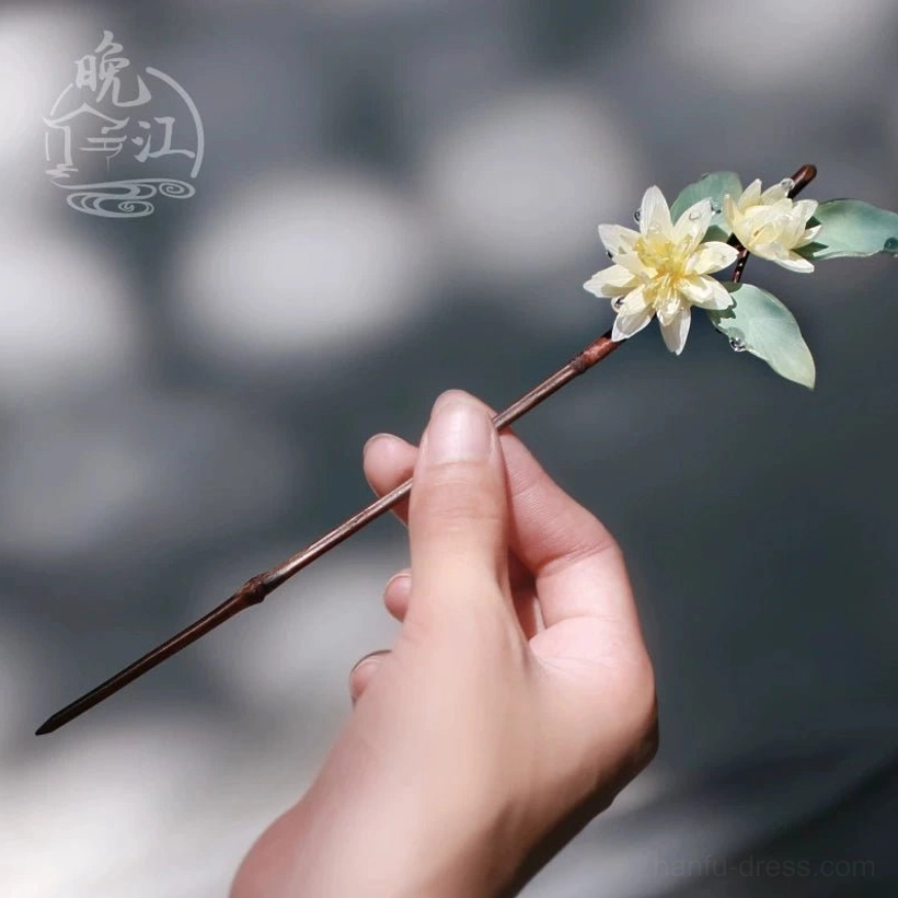 Hand holding a lotus flower Chinese hair stick with cream blossoms green foliage water drop decorations and reddish brown wooden stem