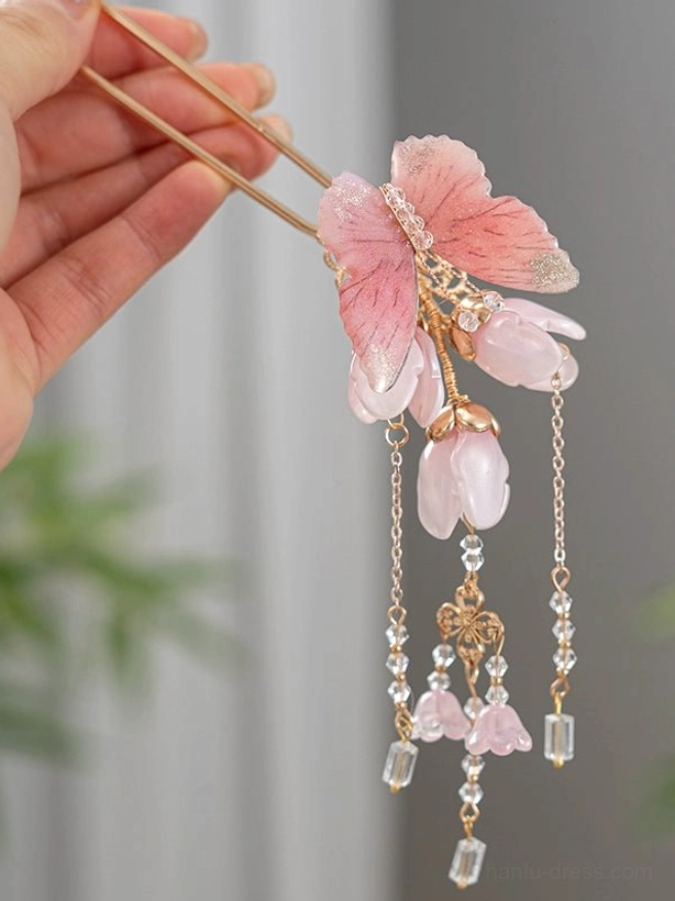Hand-held side view of a pink magnolia butterfly Chinese hair stick showing its decorative tassel structure and crystal beads