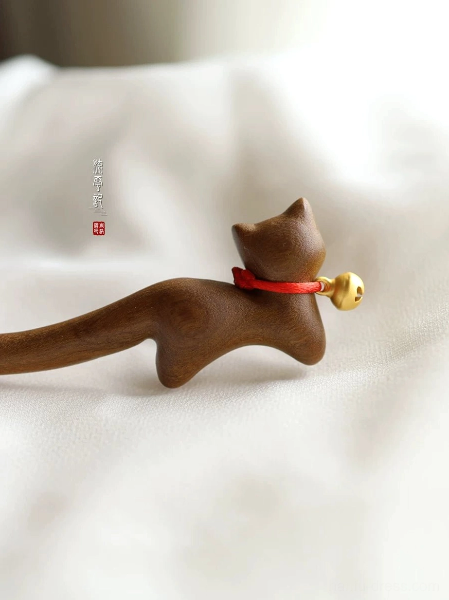 Front three-quarter view of a handmade brown wooden cat hair stick with polished finish, red neck strap, and decorative golden bell