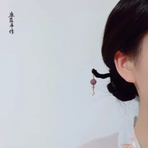 Woman wearing a handmade Chinese hair stick in a neat low bun with a dangling purple bead and pearl pendant, styled with a light Hanfu-inspired top