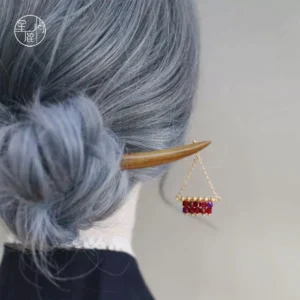 Rear view of a woman wearing a curved natural wood Chinese hair stick in an ash blue low bun, decorated with a gold chain and wine red crystal pendant for Hanfu styling