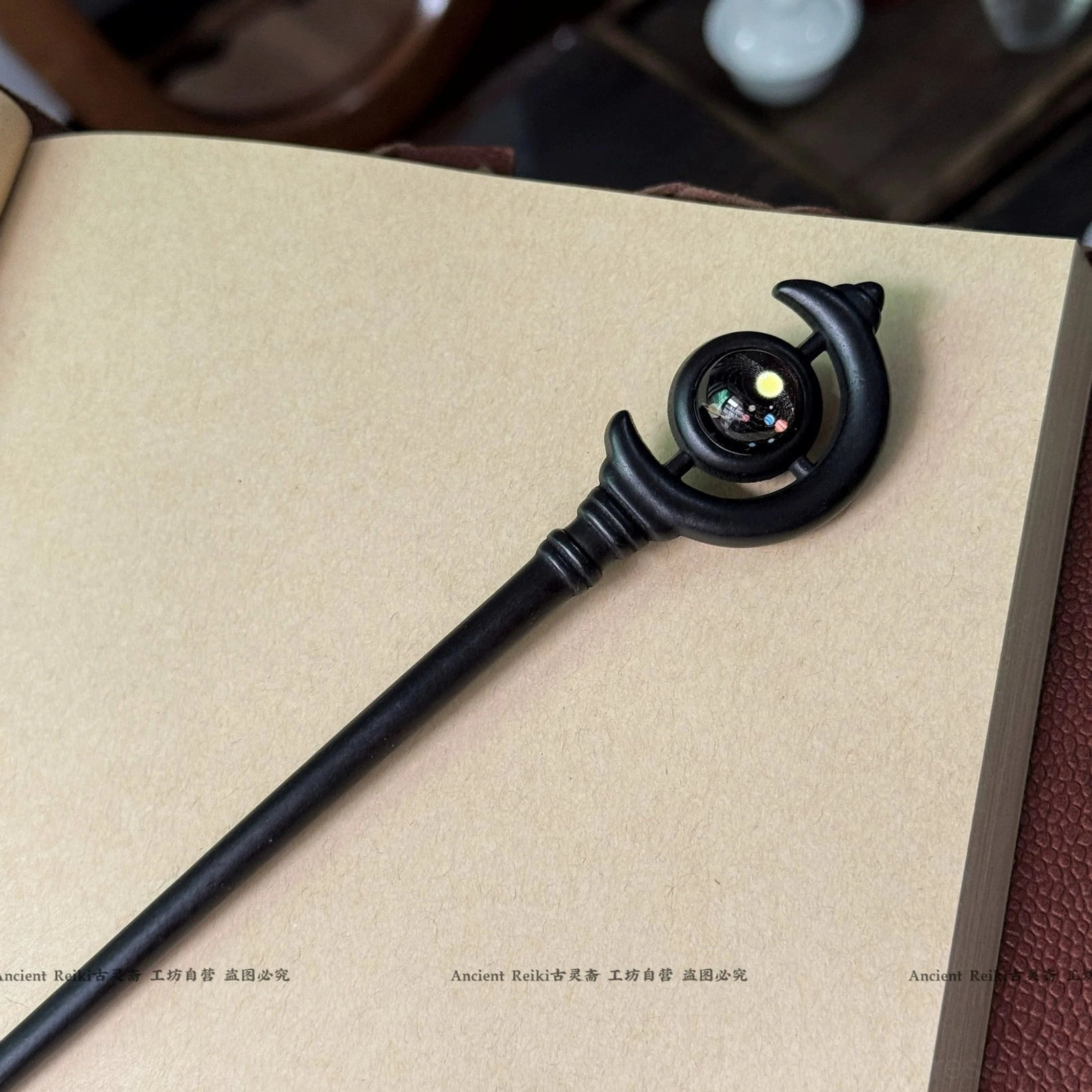 Handmade traditional Chinese hair stick with twisted decorative joint, crescent ornament, and colorful bead photographed with leather and tea ware