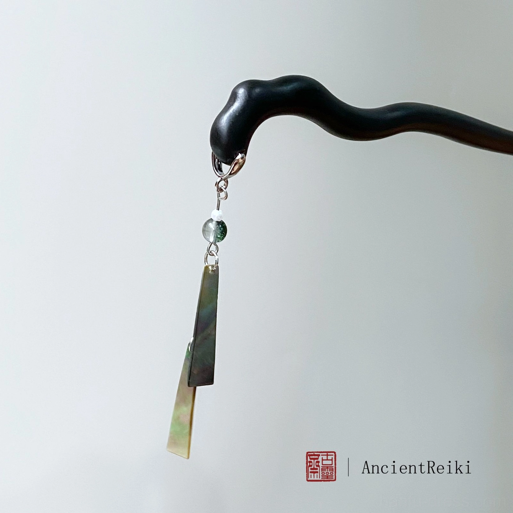 Detailed front display of a Chinese hair stick with wavy matte black wood, dual-tone green sheet pendants, silver hardware, and a dangling green round bead tassel