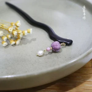 Handmade ebony Chinese hair stick with wavy dark wood design, purple pumpkin bead, pink bead, white pearl pendant, and gold-tone details displayed with dried flowers