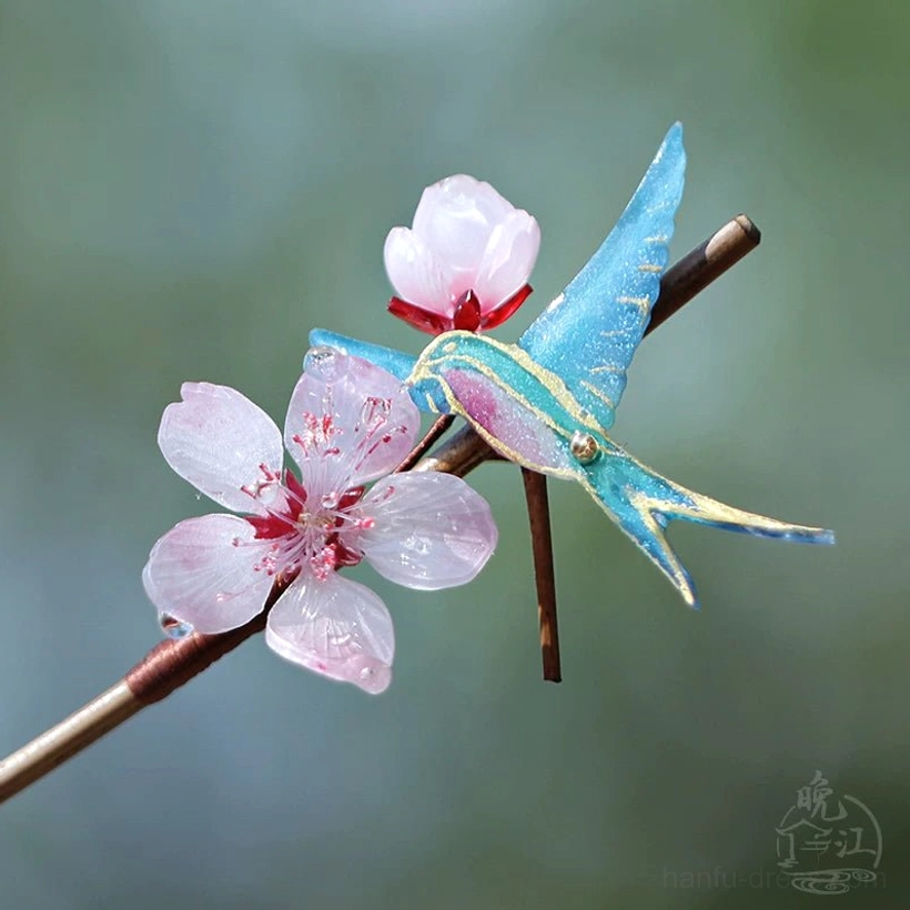 Front-side view of a handmade swallow peach blossom hair stick with an iridescent blue bird, full pink flower, flower bud, and polished wooden shaft