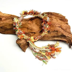 Handwoven Tibetan-inspired knot Chinese bracelet with warm mixed-colour woven cords, frayed ring edges, and a flowing multicolour tassel displayed beside natural wood