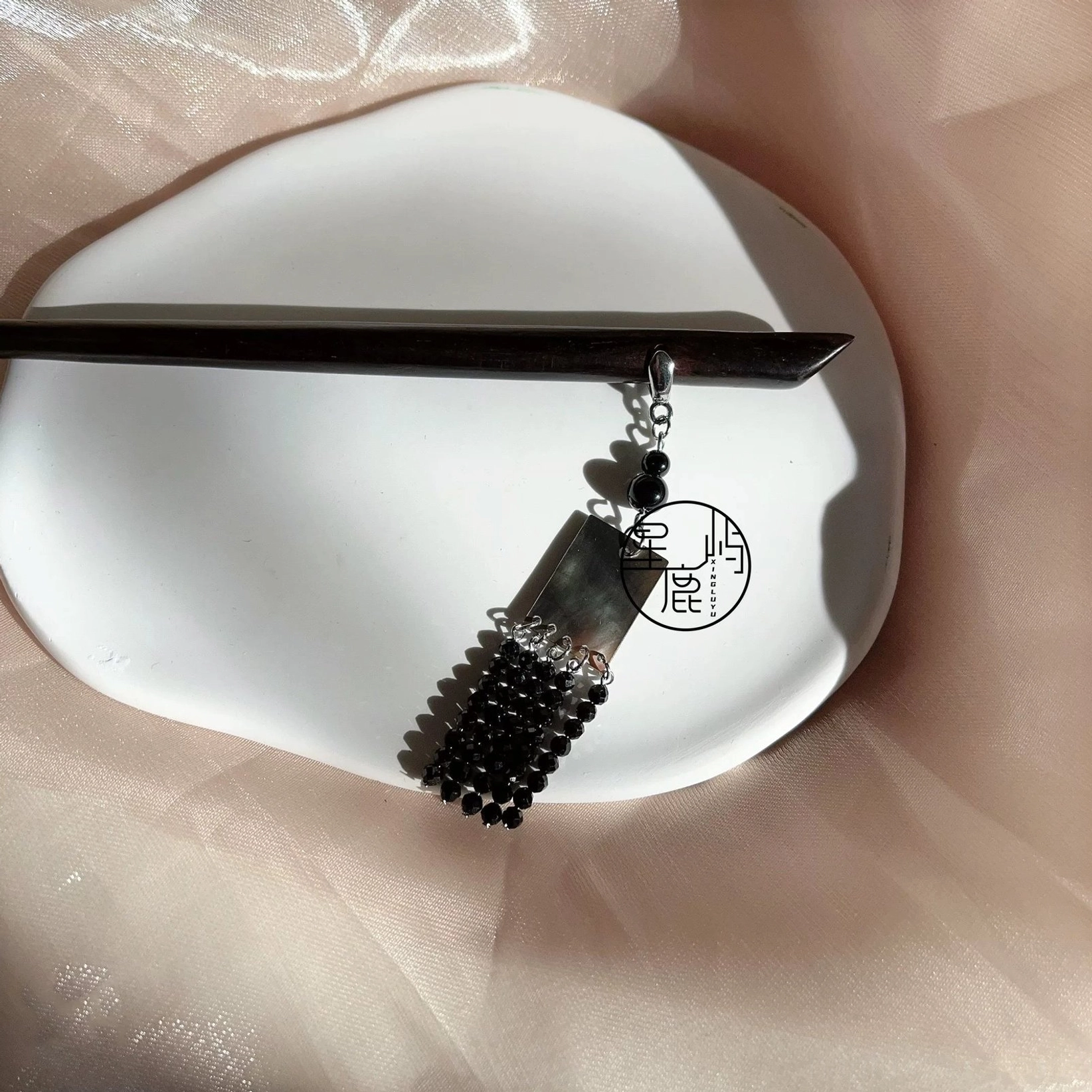 Hanfu Chinese hair stick with dark wood pin, silver-tone chain, black beads, square charm, and tassel pendant displayed on ceramic dish