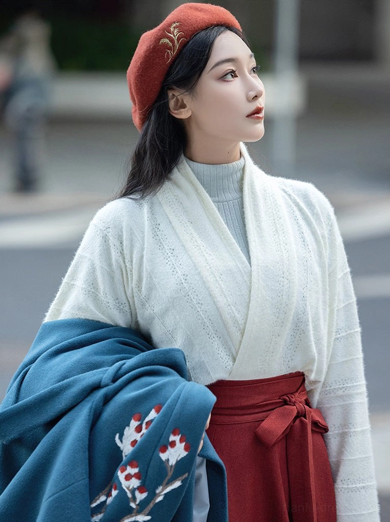 Close-up styling view of an off-white cross-collar Hanfu knit top, burgundy wrap skirt with waist tie, and dark teal embroidered beizi coat draped over the arm