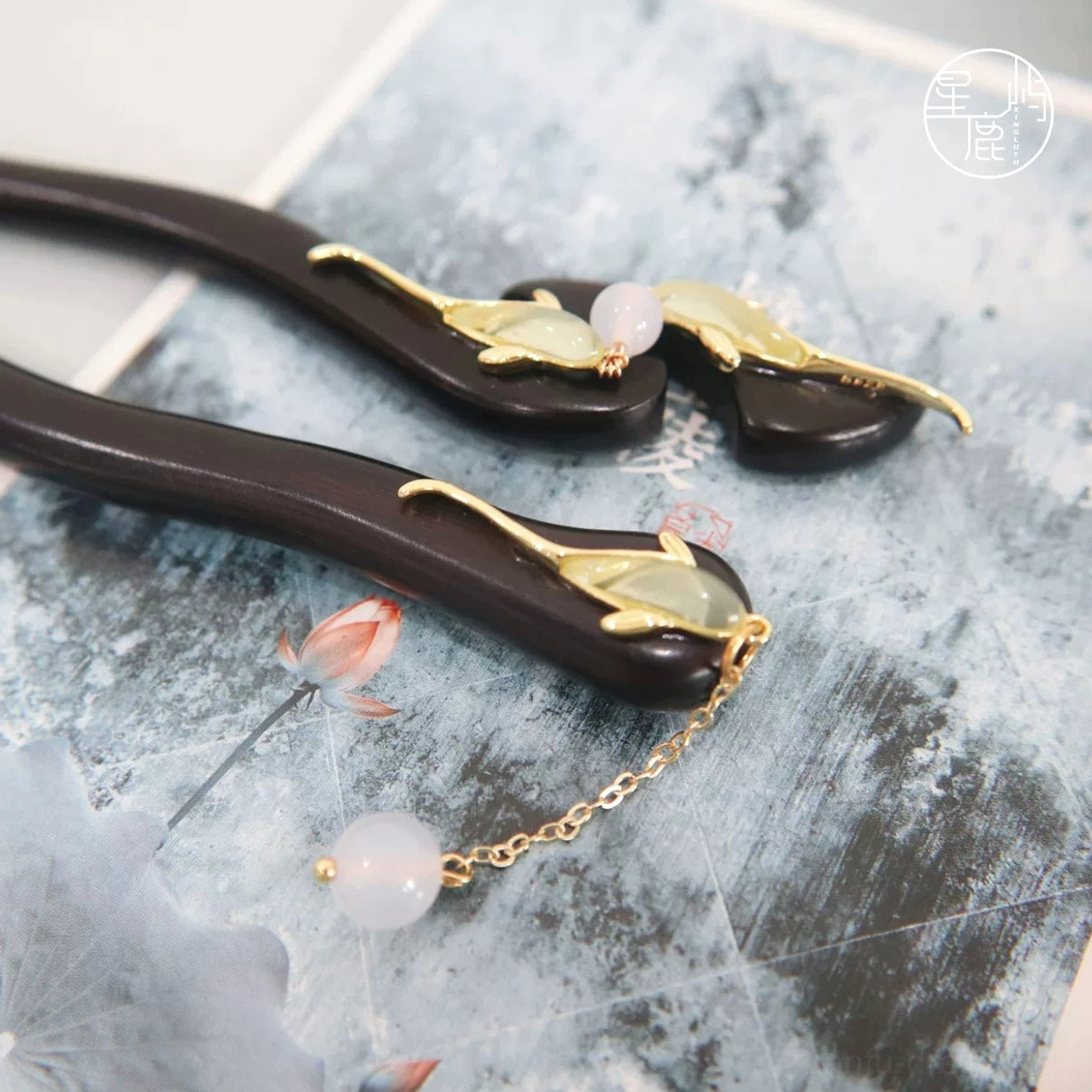 Traditional Hanfu fish hair sticks displayed on a Chinese lotus ink painting background with gold ornaments, white beads, and decorative tassel