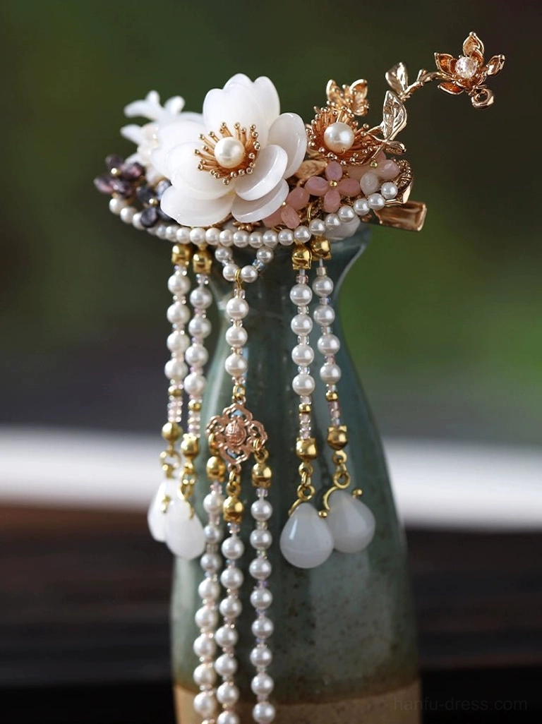 Intricate Hanfu floral hairpin with pink gemstone accents gold-tone details and layered pearl tassels displayed on a green ceramic vase