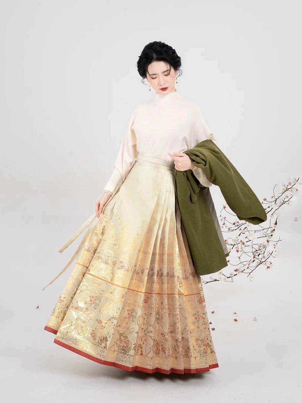 Hanfu model walking in a gold-patterned mamian skirt while carrying an olive-green embroidered coat