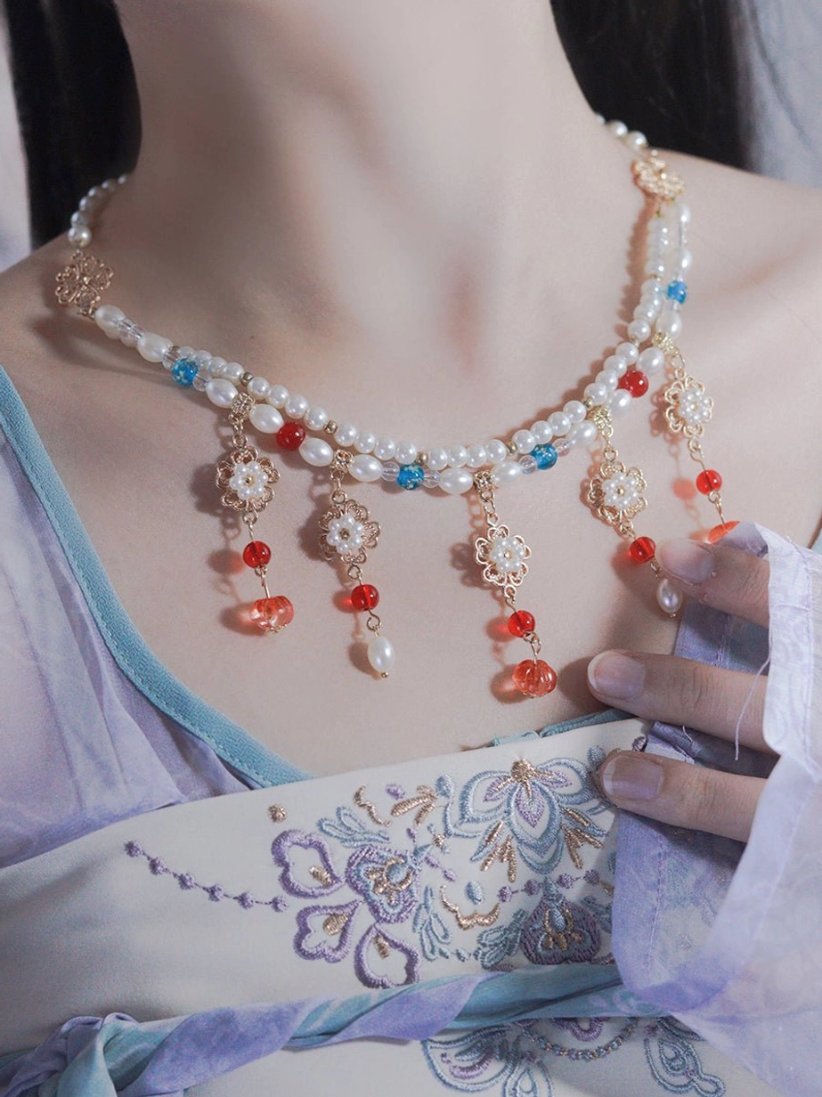 Female model wearing a traditional Chinese Hanfu necklace with layered pearl chains, colorful beads, gold floral ornaments, and tassel pendants over a purple embroidered Hanfu top