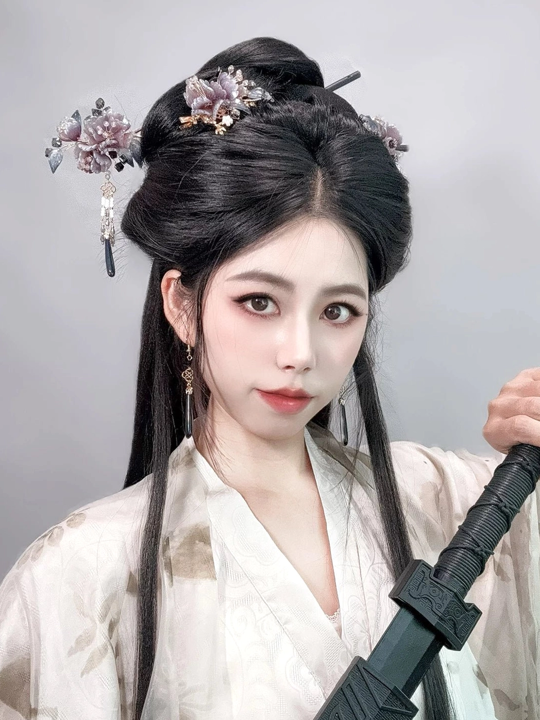 Hanfu outfit styled with multiple mauve peony Chinese hair sticks and blue tassel ornaments in a classical updo while holding a traditional sword