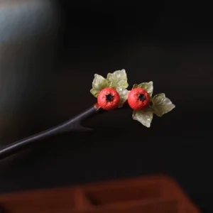 Close-up side view of a dark wood Chinese hair stick with vivid red simulated hawthorn berries and translucent green leaves