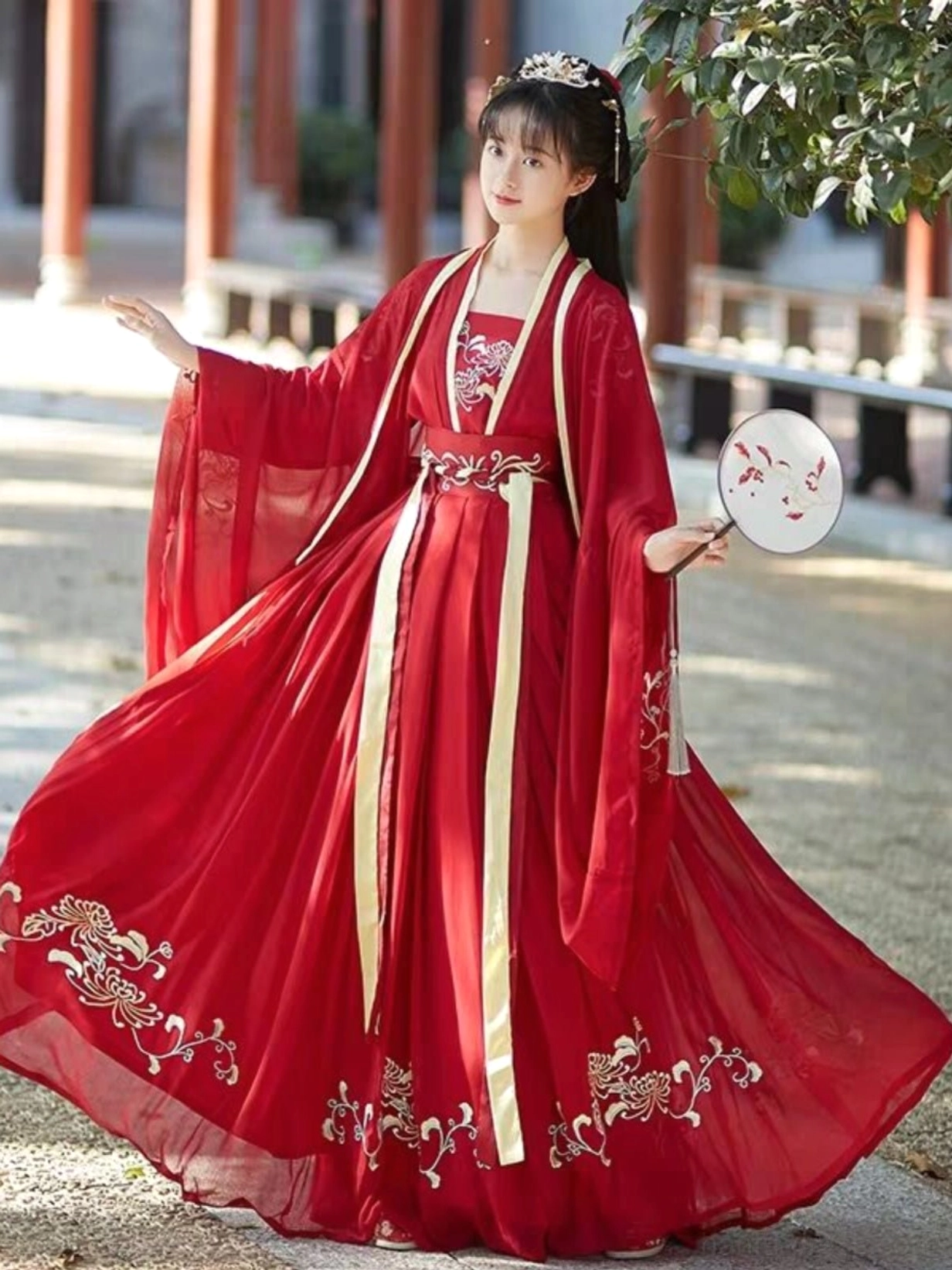 Red floral embroidered Song Dynasty style qiyao ruqun hanfu with yellow waist trim, wide sleeves, and round silk fan in Chinese courtyard