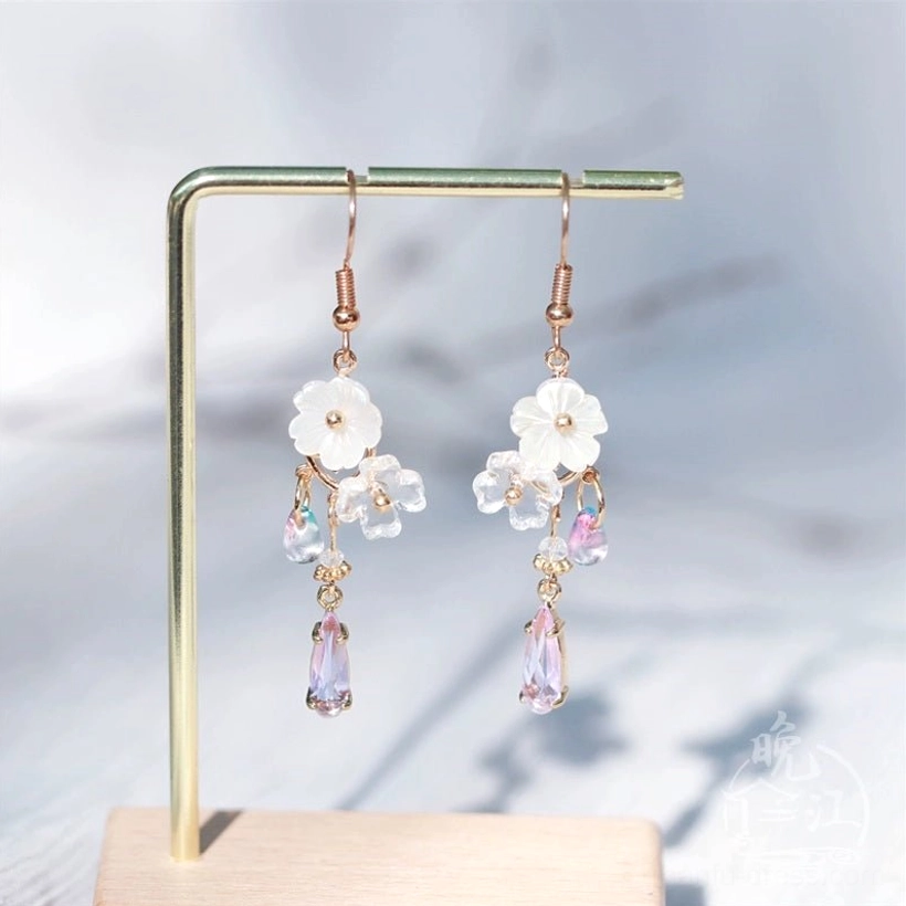 Hua Luo floral shell and purple teardrop Chinese earrings displayed on a metal jewelry stand with rose gold hook wires