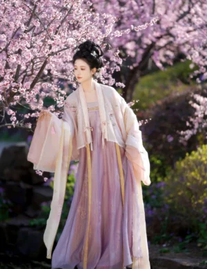 Hundred Flowers Scroll Tang Dynasty hanfu set with pastel pink embroidered wide-sleeve cardigan, lavender qixiong skirt and shawl photographed beneath blooming cherry blossoms
