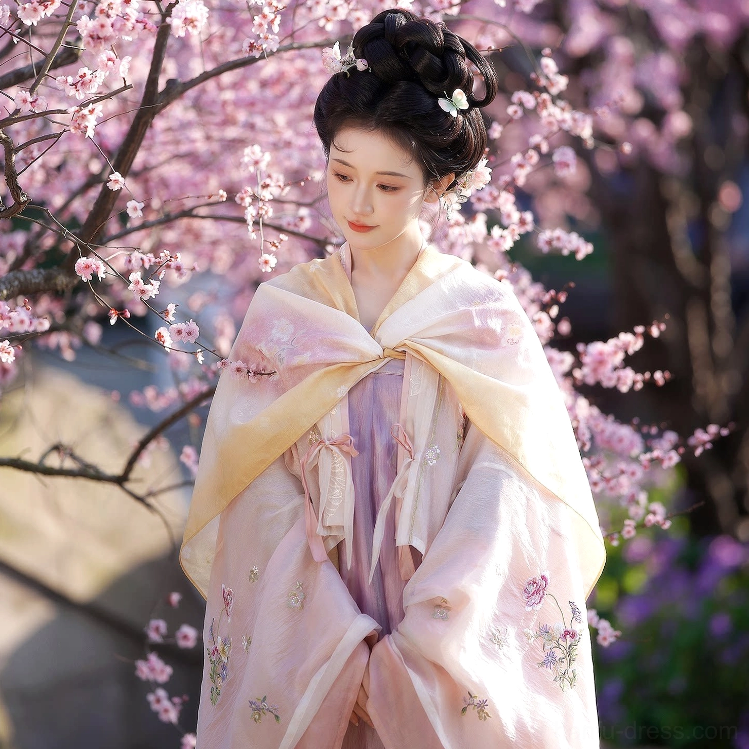 Close three-quarter view of Tang Dynasty hanfu with floral pink robe, yellow-trimmed shoulder shawl, lavender qixiong skirt and traditional Tang-style hairstyle among flower branches